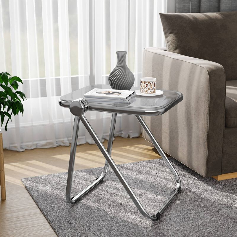 LeisureMod Lawrence Mid-Century Modern Rectangular Folding Side Table in Chrome Finish with Plastic Tabletop and Aluminum Frame Transparent Black by Couch.