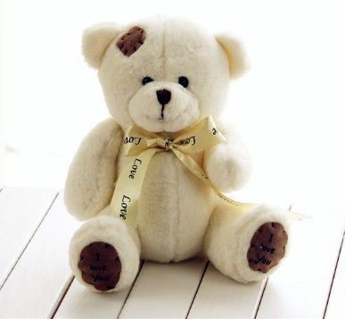 White teddy bear with a yellow ribbon on a white wooden surface.