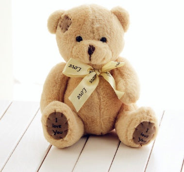 Teddy bear with a I love you'bow on a white wooden surface.