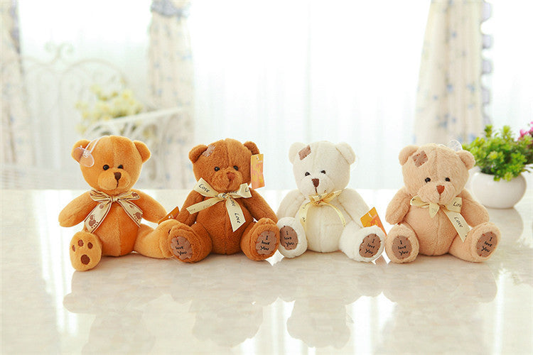 Four teddy bears of different colors sitting on a light surface with a blurred background.