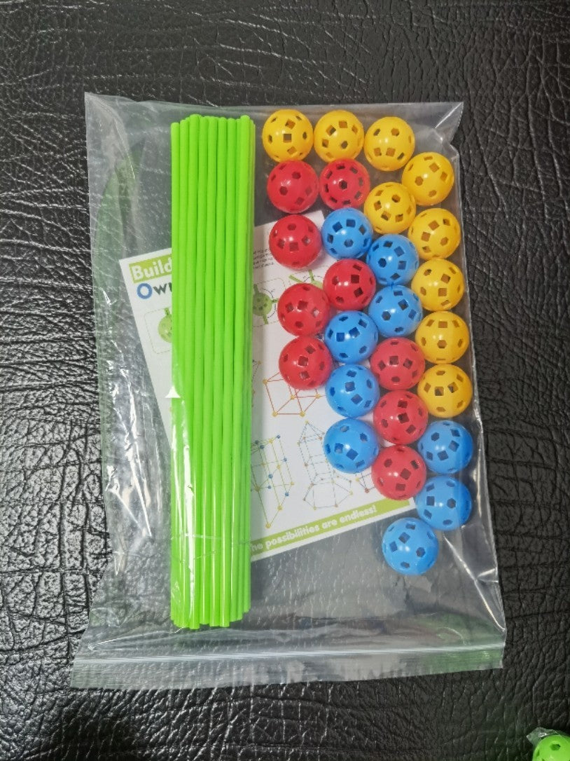 Colorful plastic balls and green sticks in a clear bag on a textured black surface.