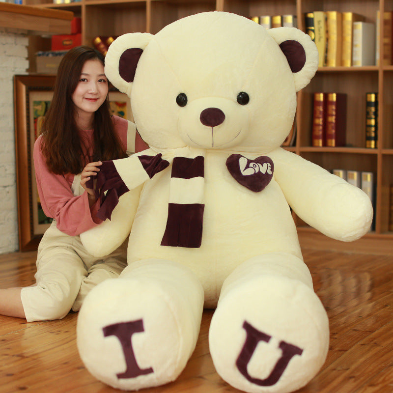 Large white teddy bear with brown accents and letters I and U held by a person in a cozy room.