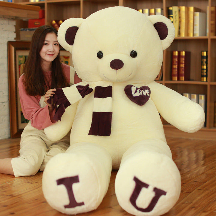 Large white teddy bear with brown accents and letters I and U held by a person in a cozy room.