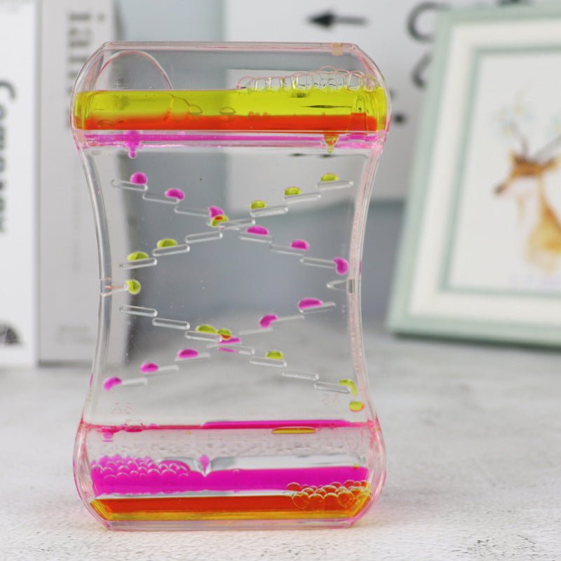 Transparent container with colorful liquid and beads on a light surface.