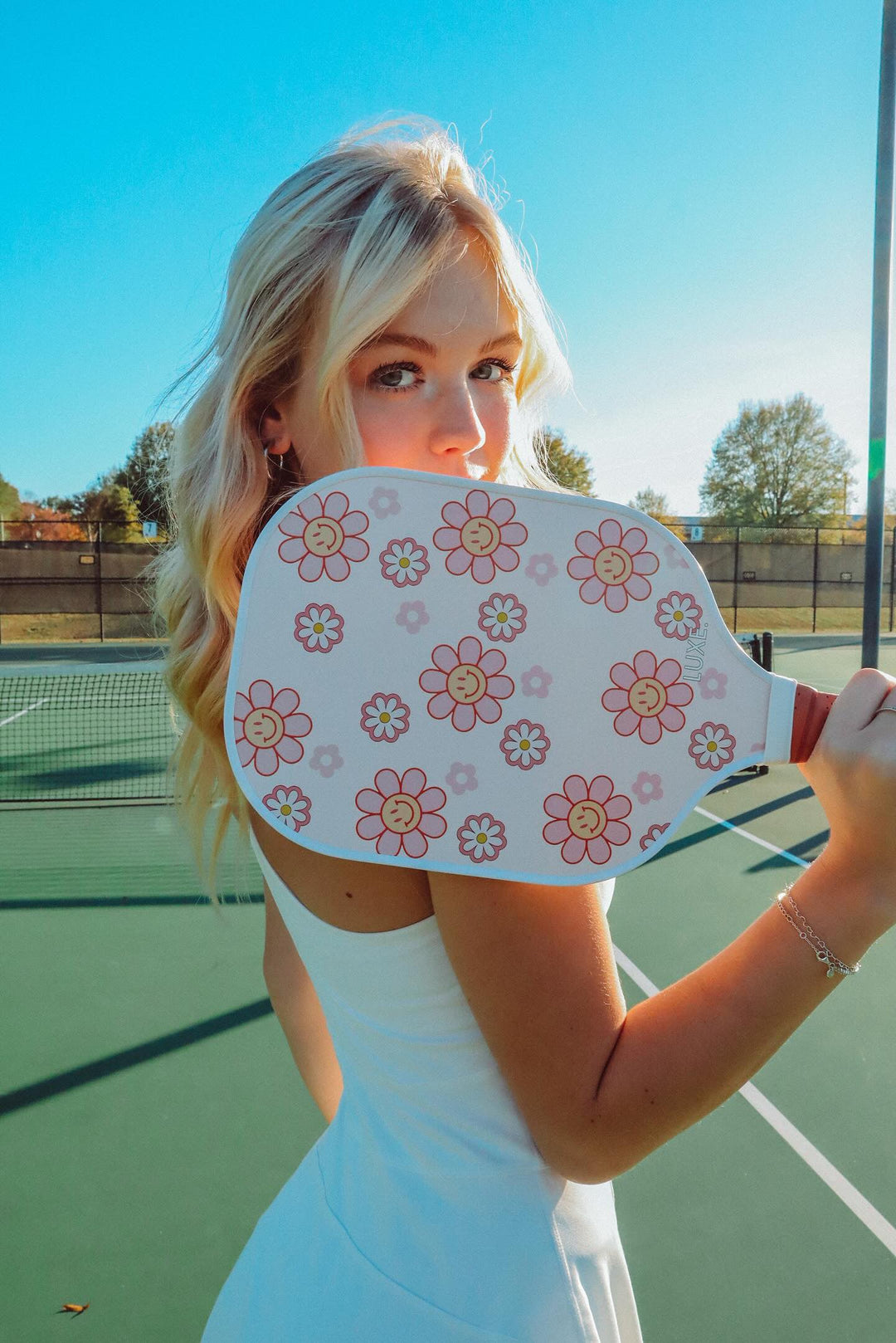 Woman holding a pink paddle with floral designs on a tennis court.