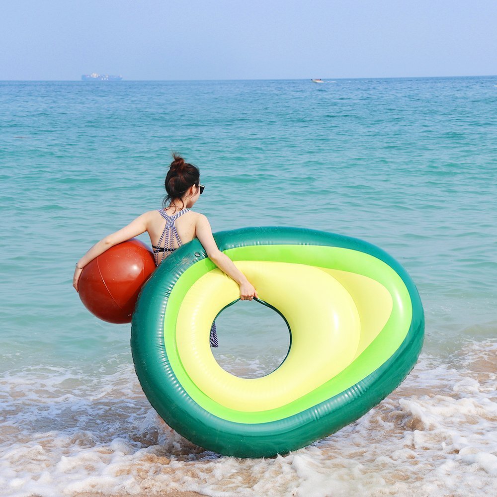 Woman holding an avocado-shaped inflatable pool toy in the ocean.