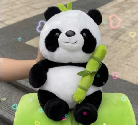 Plush panda toy holding a bamboo stick on a green cushion with a blurred background.