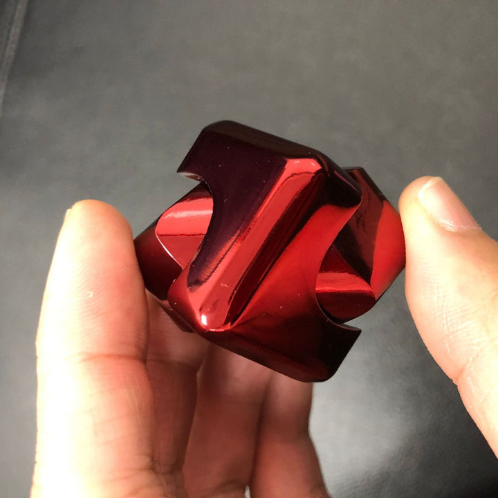 Red metallic object held between fingers against a dark background.
