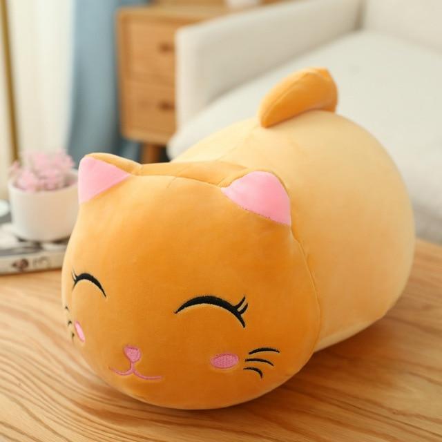Plush cat-shaped pillow on a wooden surface with a blurred indoor background.