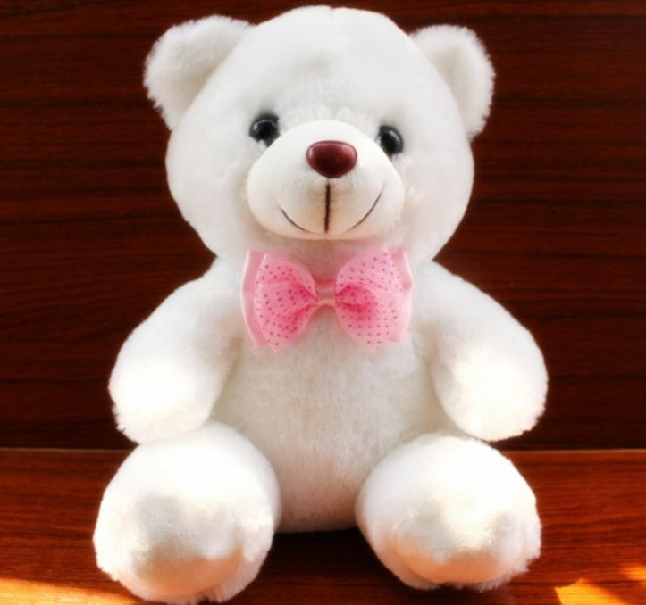 White teddy bear with a pink bow tie on a wooden surface.