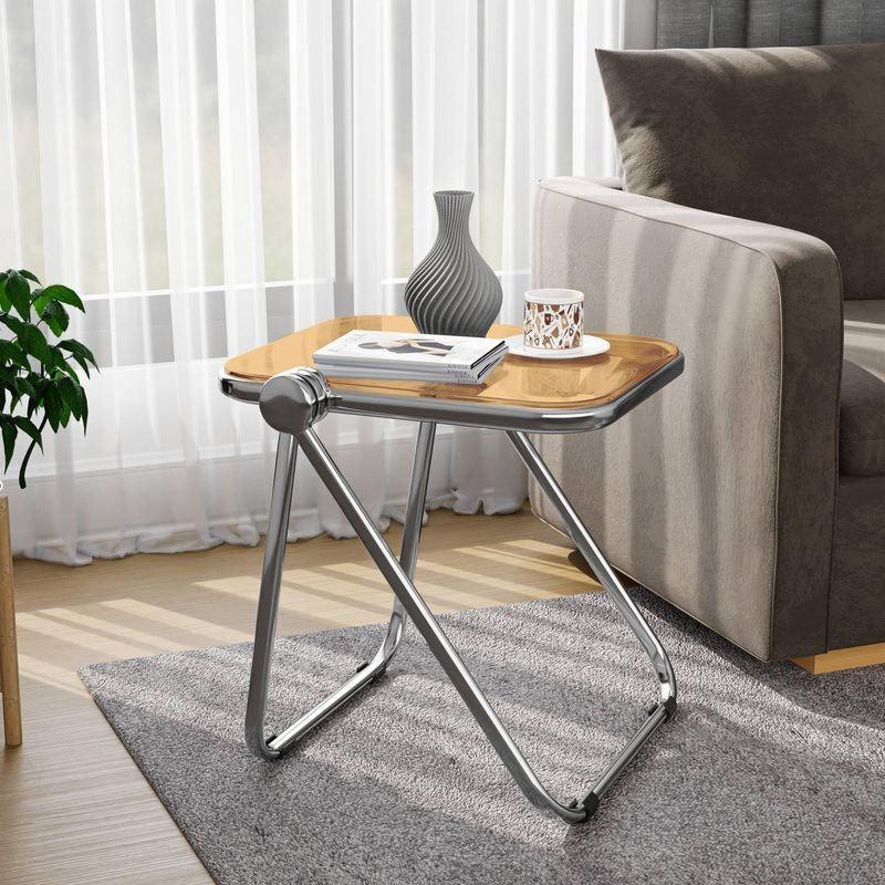 LeisureMod Lawrence Mid-Century Modern Rectangular Folding Side Table in Chrome Finish with Plastic Tabletop and Aluminum Frame Orange by Couch.