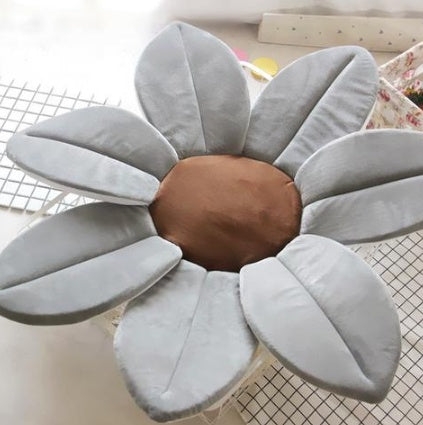 Flower shaped cushion with gray petals and a brown center on a checkered floor.
