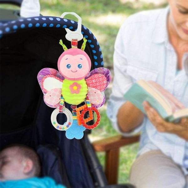 Butterfly-shaped baby toy hanging from a stroller with a blurred background of a person reading.
