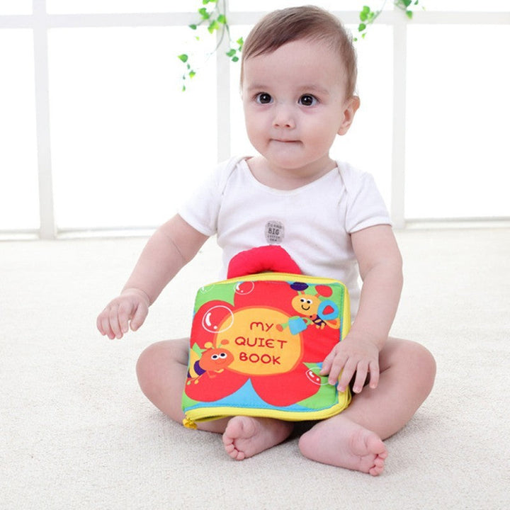 Baby holding a colorful soft book with a white background.