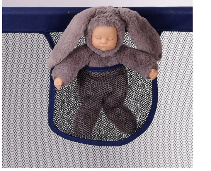 Baby doll in a bunny costume inside a mesh pocket of a crib safety fence.