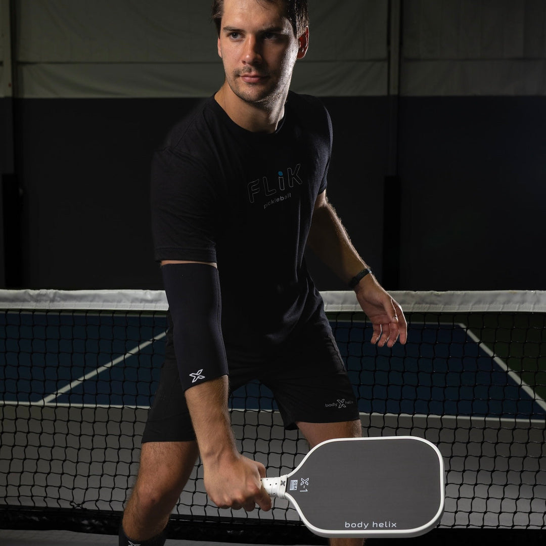 Man holding a pickleball paddle on a court with branding.