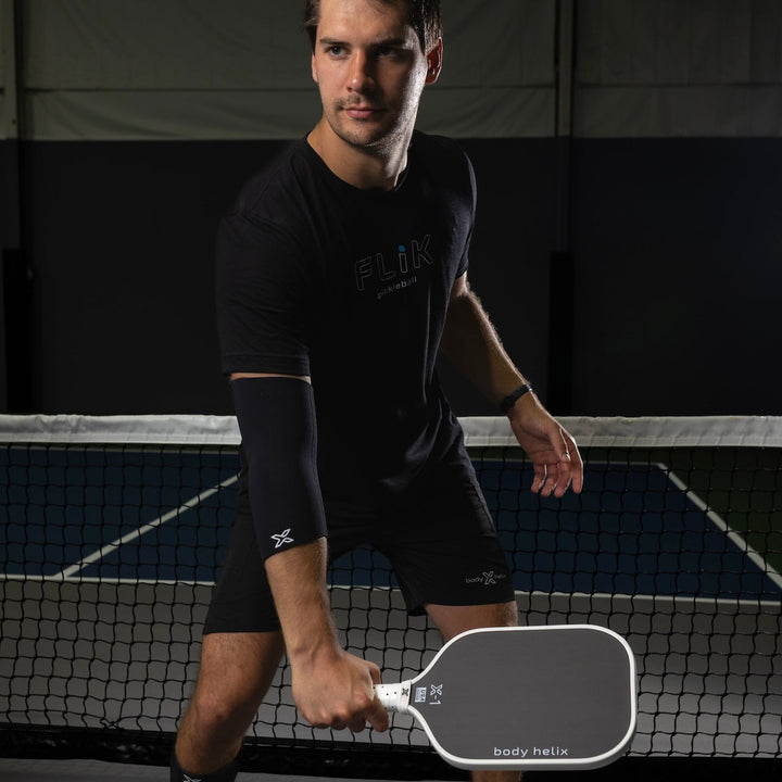 Man holding a pickleball paddle on a court with branding.