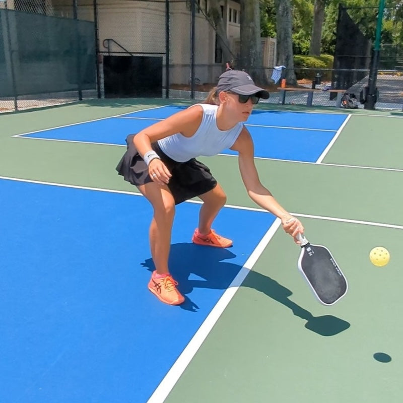 Woman playing pickleball on a court with a paddle and ball.