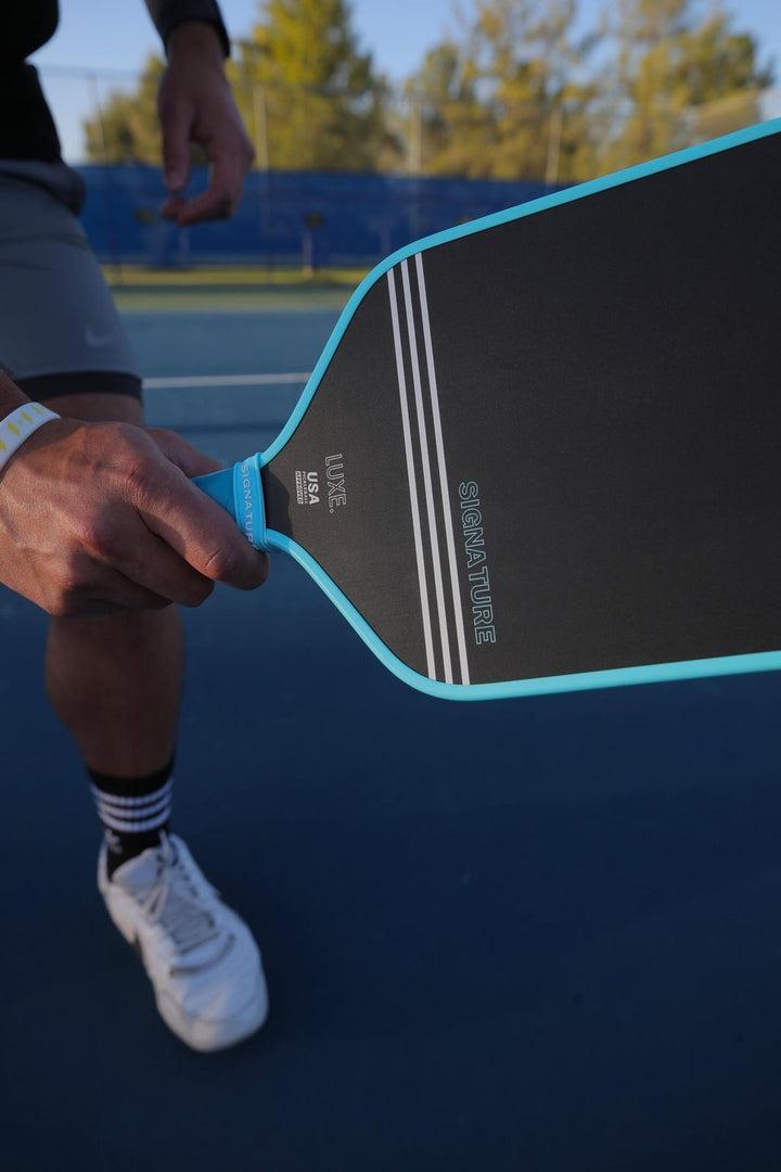 Person holding a pickleball paddle on a tennis court.