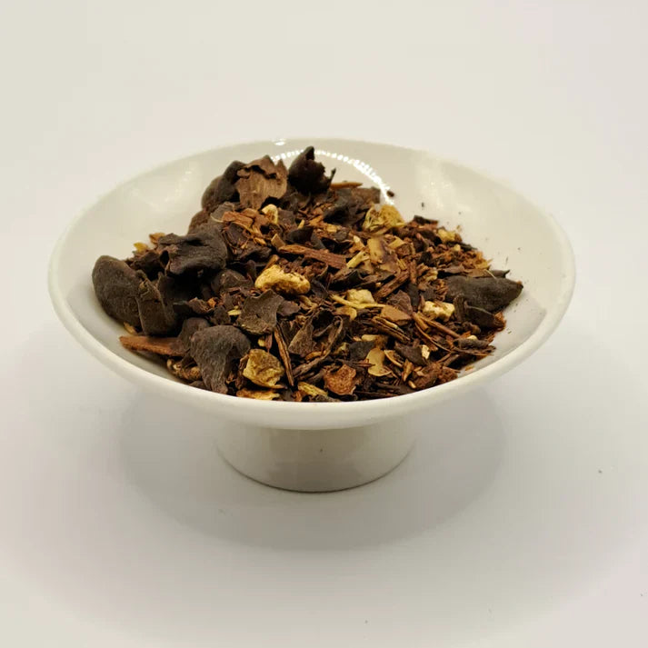 White bowl filled with dark brown leafy herbs on a white background.
