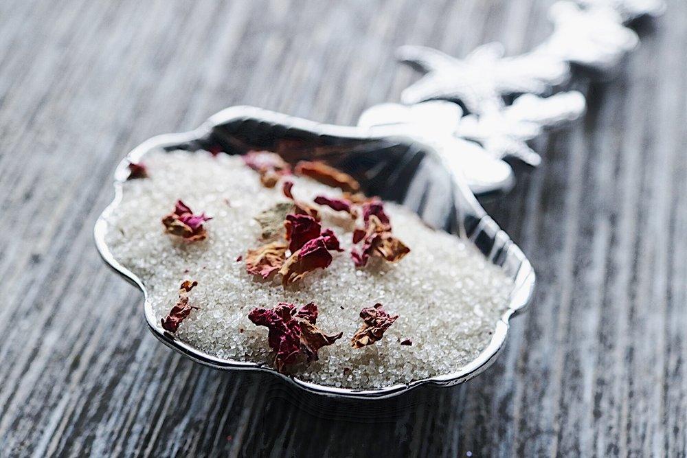 Silver spoon with sugar and dried flowers on a wooden surface.