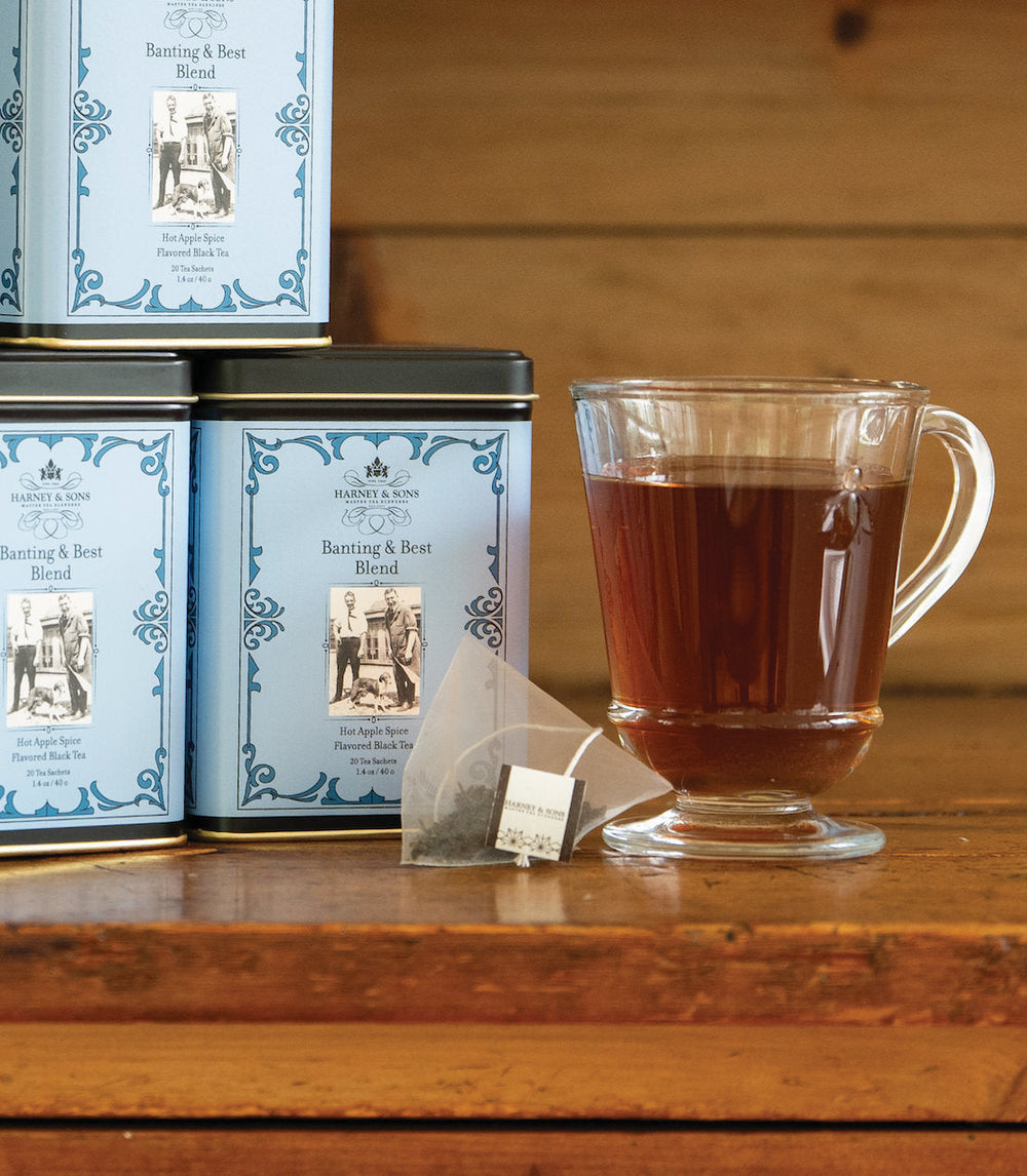 Tea canisters and a glass mug with tea on a wooden surface.