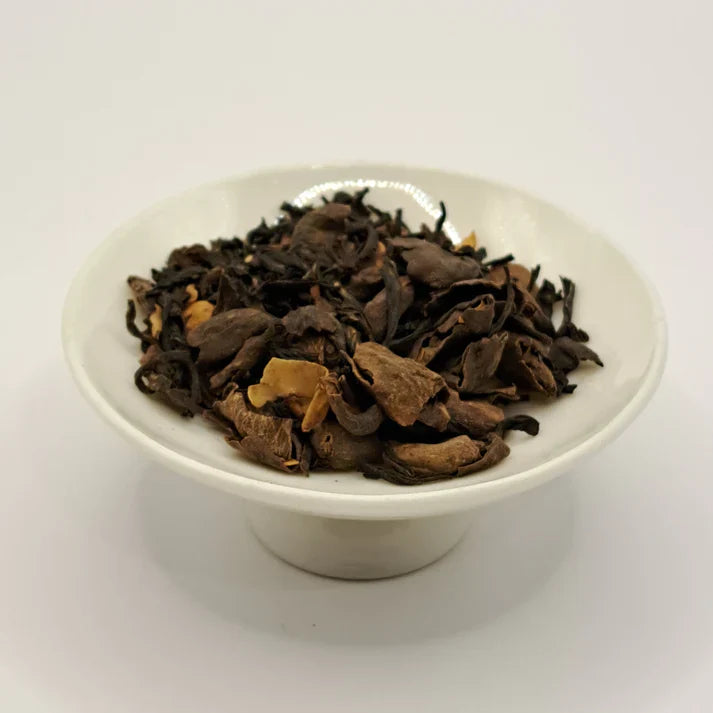 Dry black tea leaves in a white ceramic cup on a light gray background