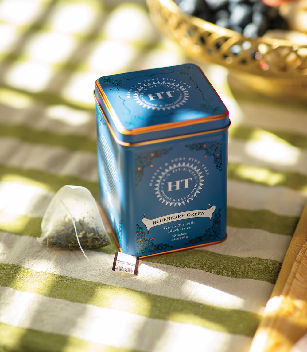 Blue tea tin with a tea bag on a striped tablecloth.