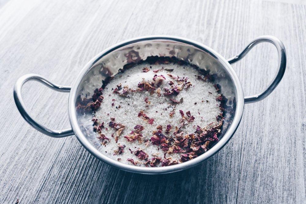 Metal colander with dried flowers and sugar on a wooden surface.