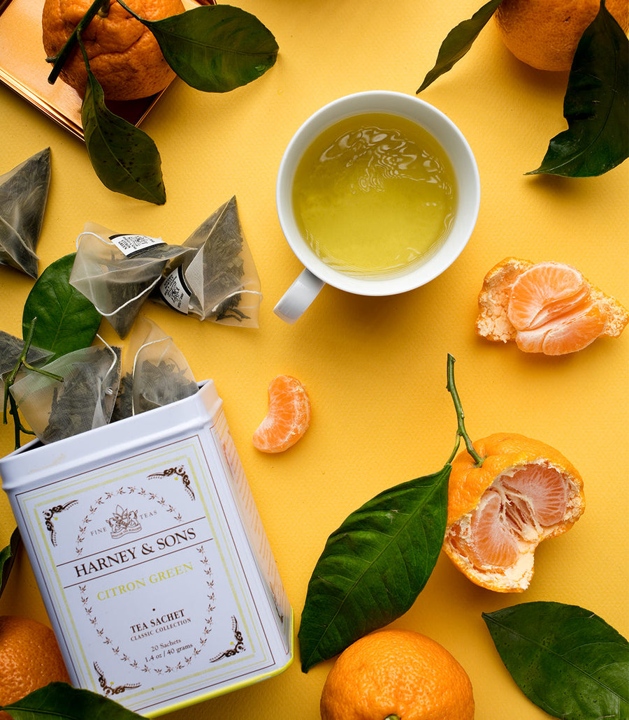Teacup with green tea, Harney and Sons tea bags, and oranges on a yellow background