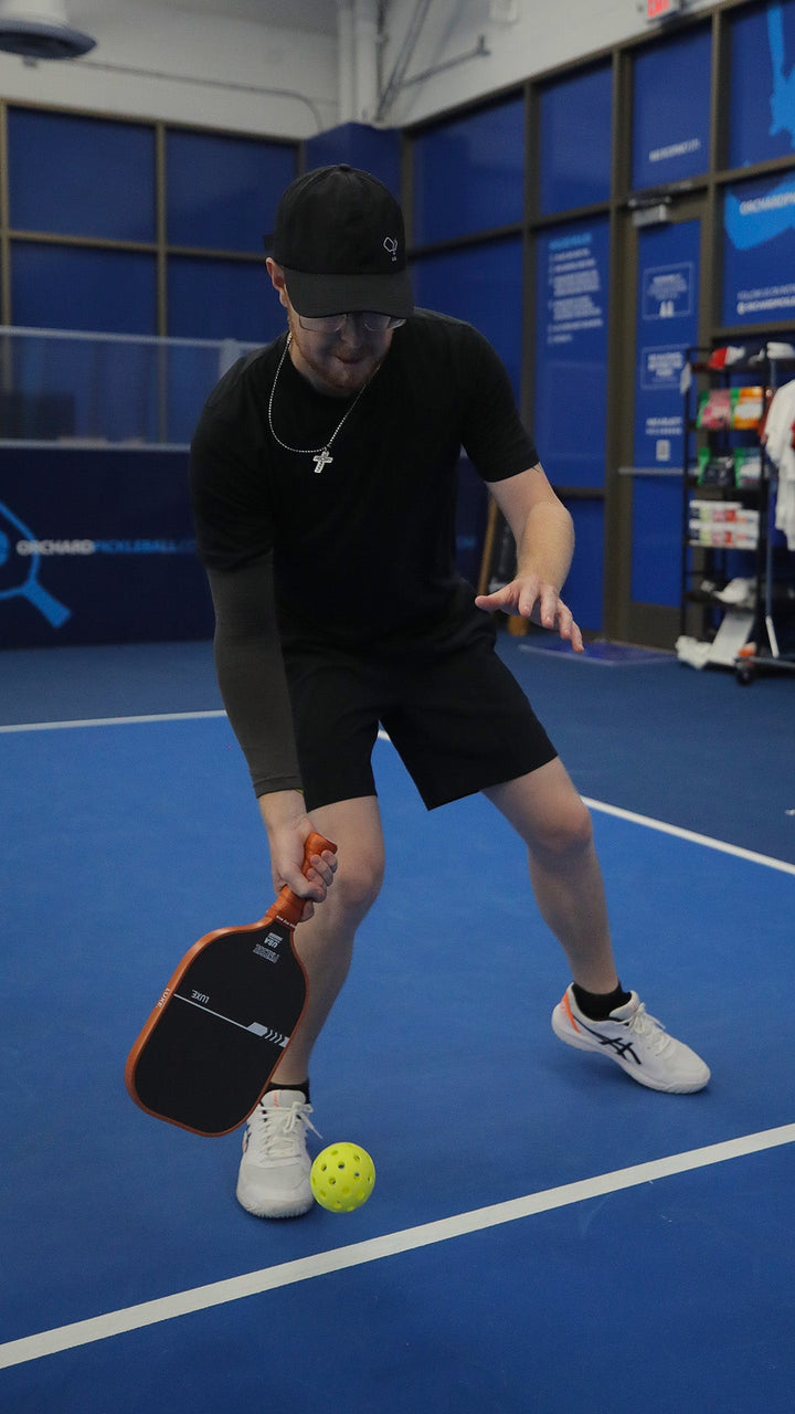 Person playing pickleball on a blue court with equipment in the background.