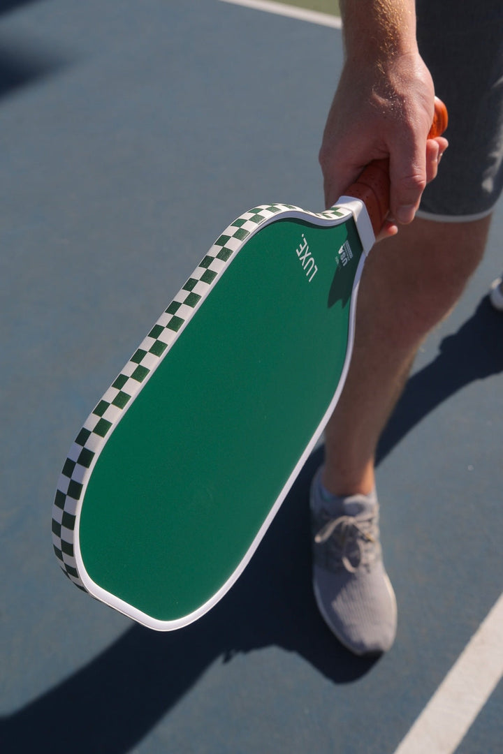 Green pickleball paddle held by a person on a court.