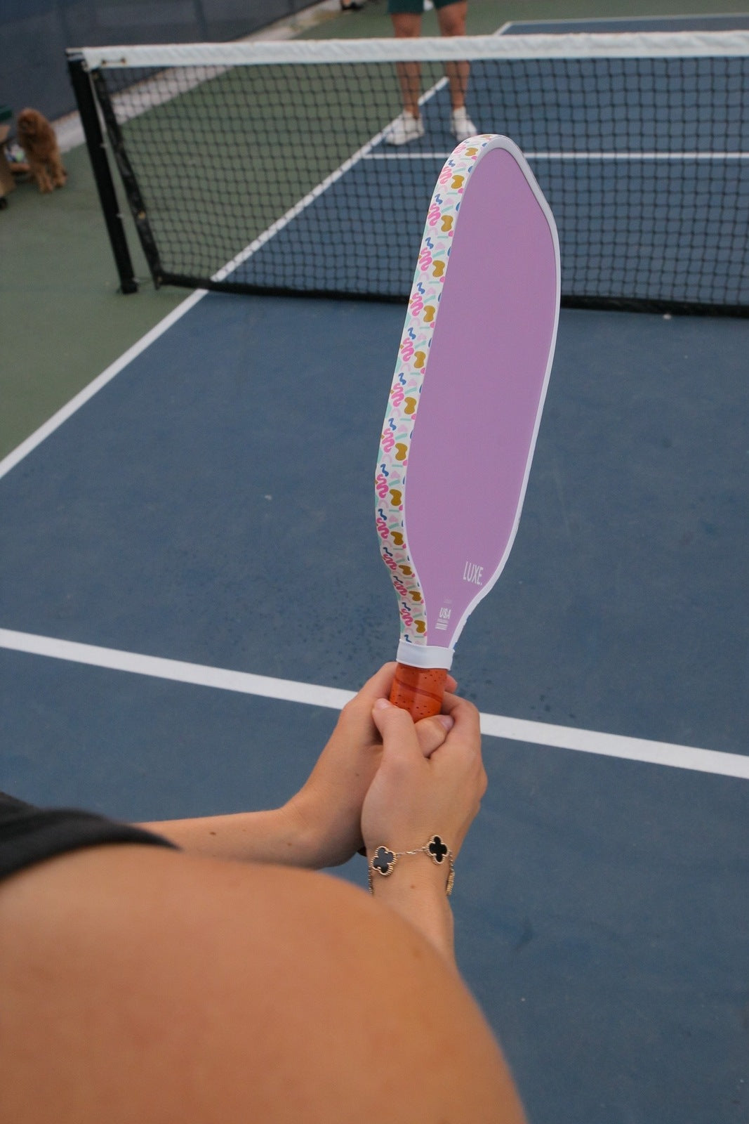 Person holding a purple paddle with a pattern on a tennis court.