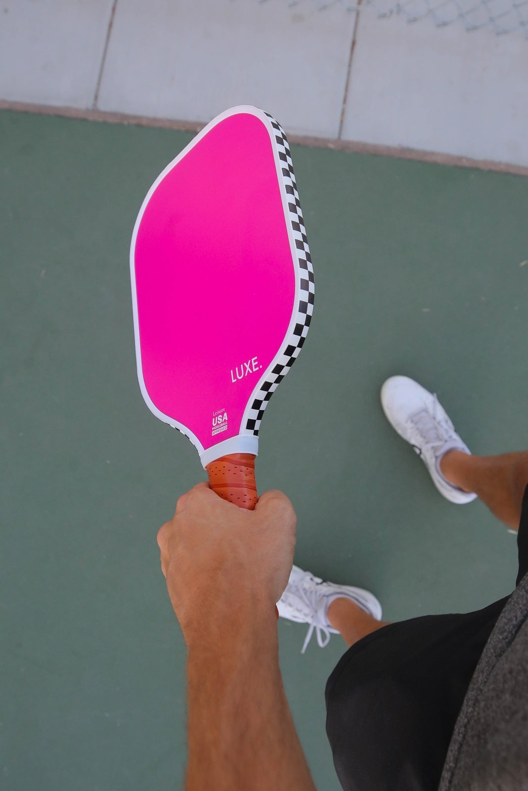 Person holding a pink pickleball paddle on a court.