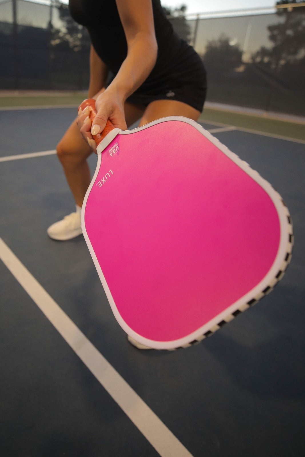 Person holding a pink pickleball paddle on a court.