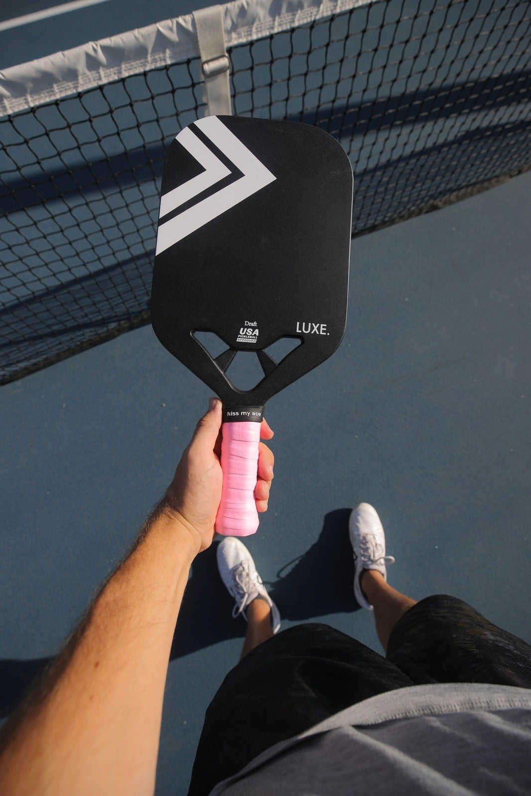 Person holding a pickleball paddle on a court with a net in the background.