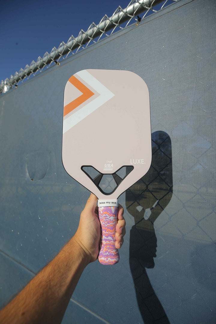 Hand holding a pink pickleball paddle against a chain-link fence background.