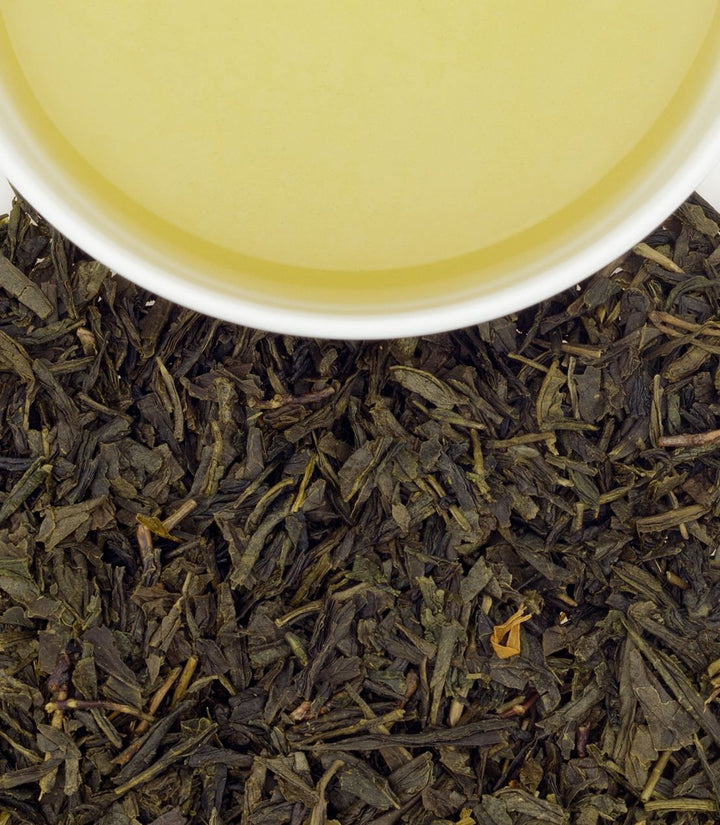 Close-up of tea leaves with a cup of tea in the background