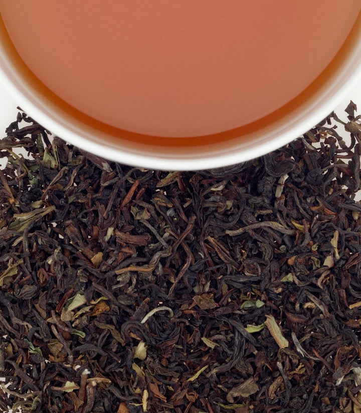 Dry tea leaves with a cup of tea in the background.