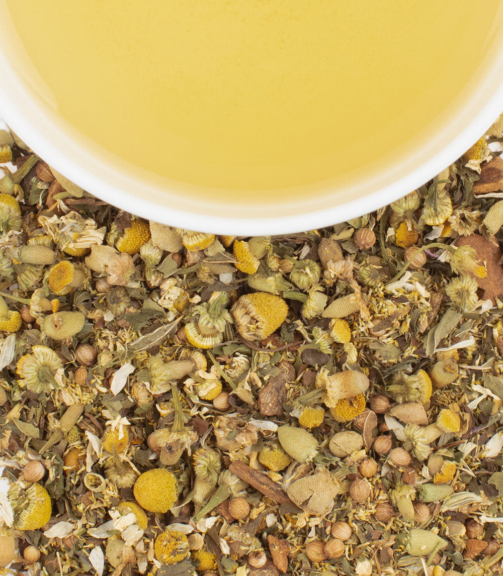 Herbal tea leaves with a cup of tea in the background.