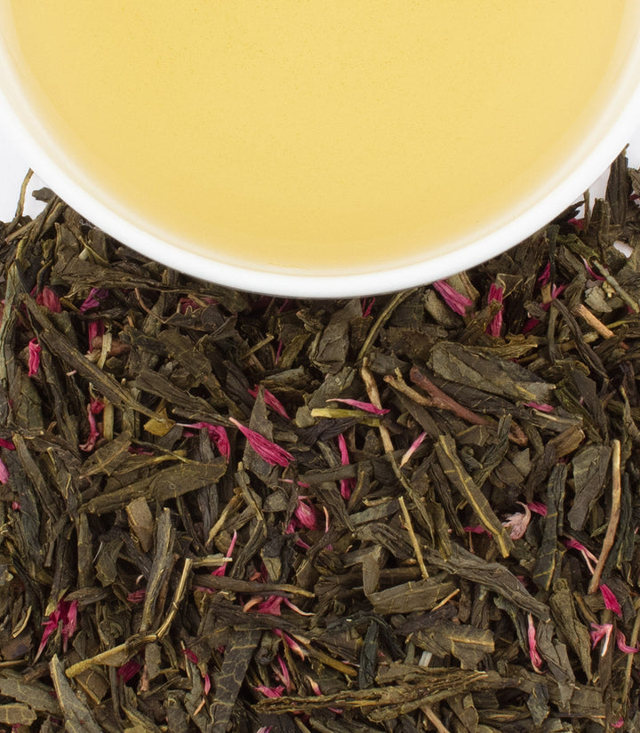 Tea leaves with a cup of tea in the background.