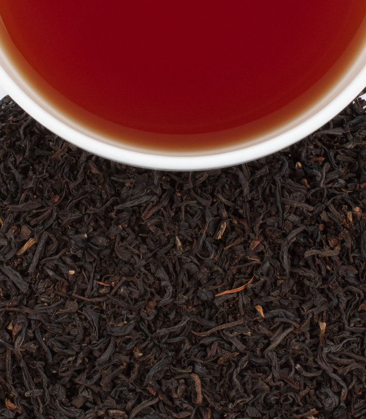 Close-up of tea leaves with a cup of tea in the background.