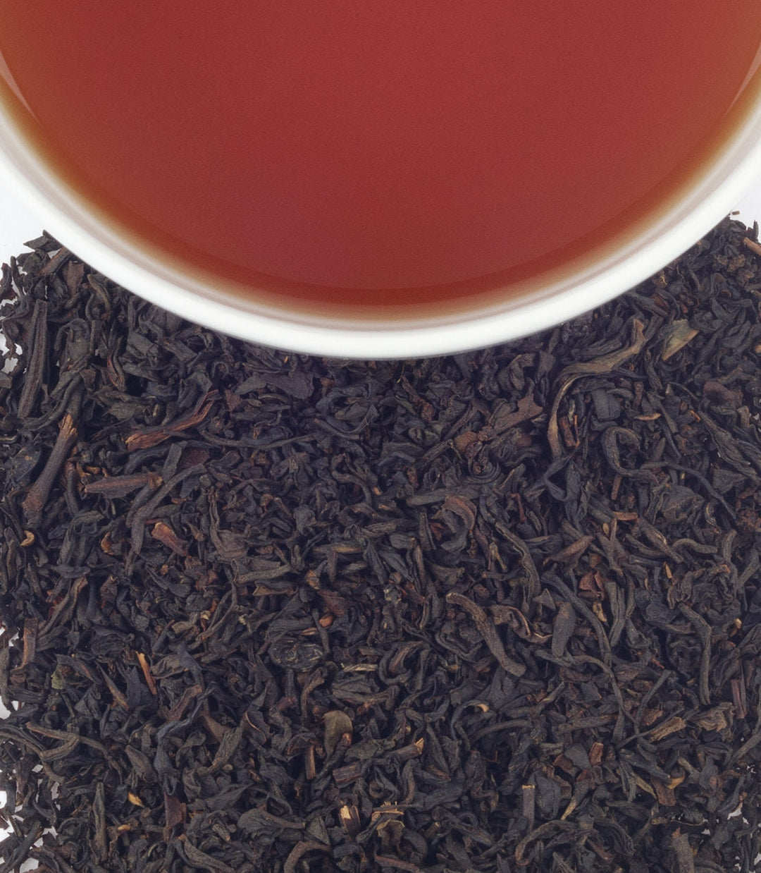 Black tea leaves with a cup of tea in the background.