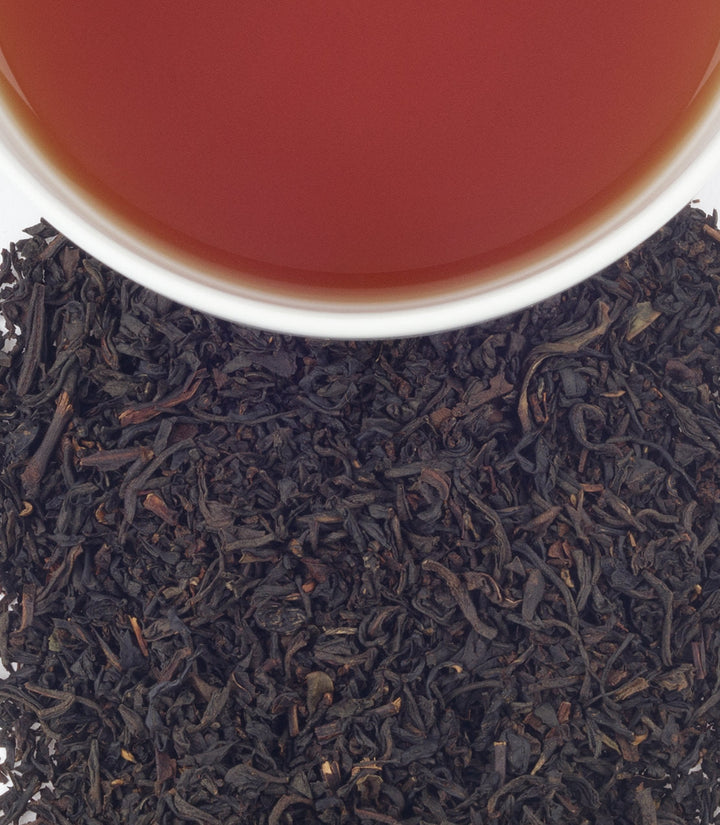 Black tea leaves with a cup of tea in the background.
