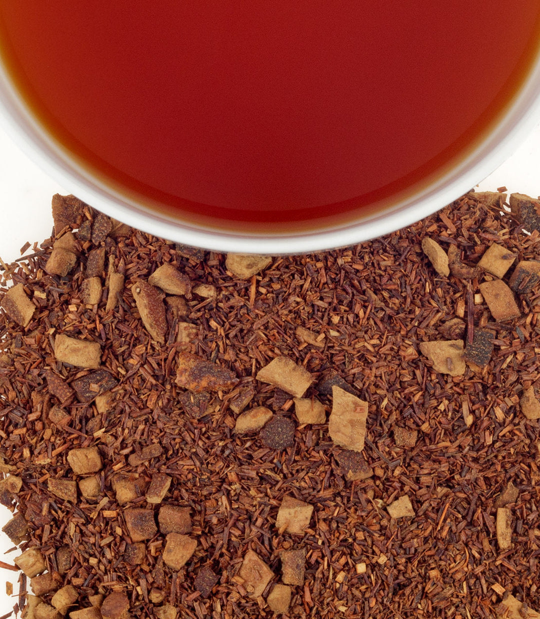 Close-up of dried rooibos tea leaves with a cup of red tea in the background.