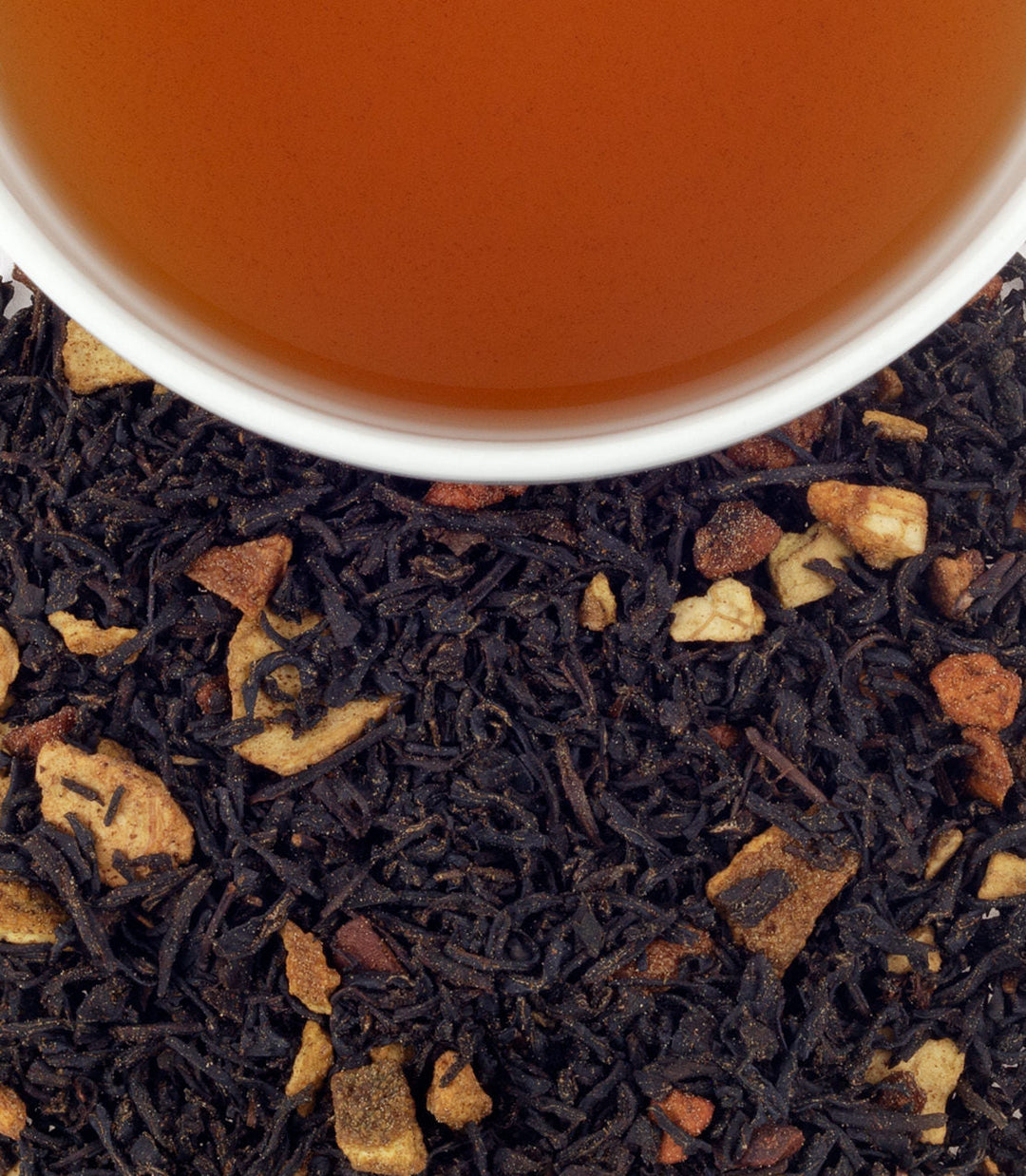 Close-up of black tea leaves with a cup of tea in the background.
