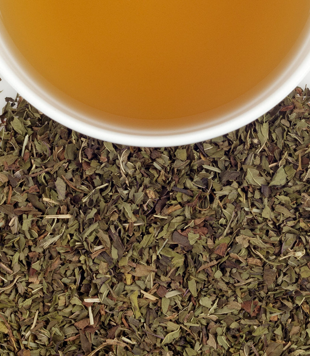 Dry tea leaves with a cup of tea above them.