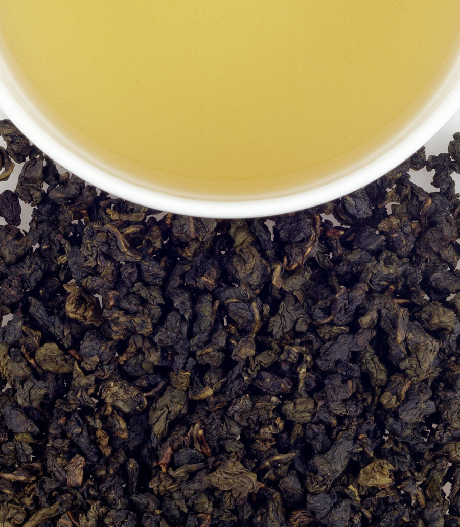 Close-up of tea leaves with a cup of tea in the background.