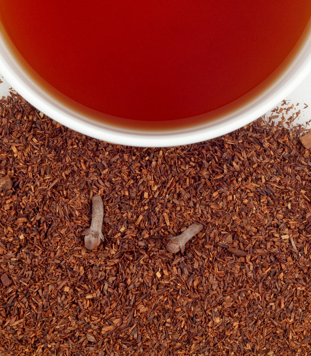 Close-up of a cup of red tea with scattered tea leaves on a white surface.