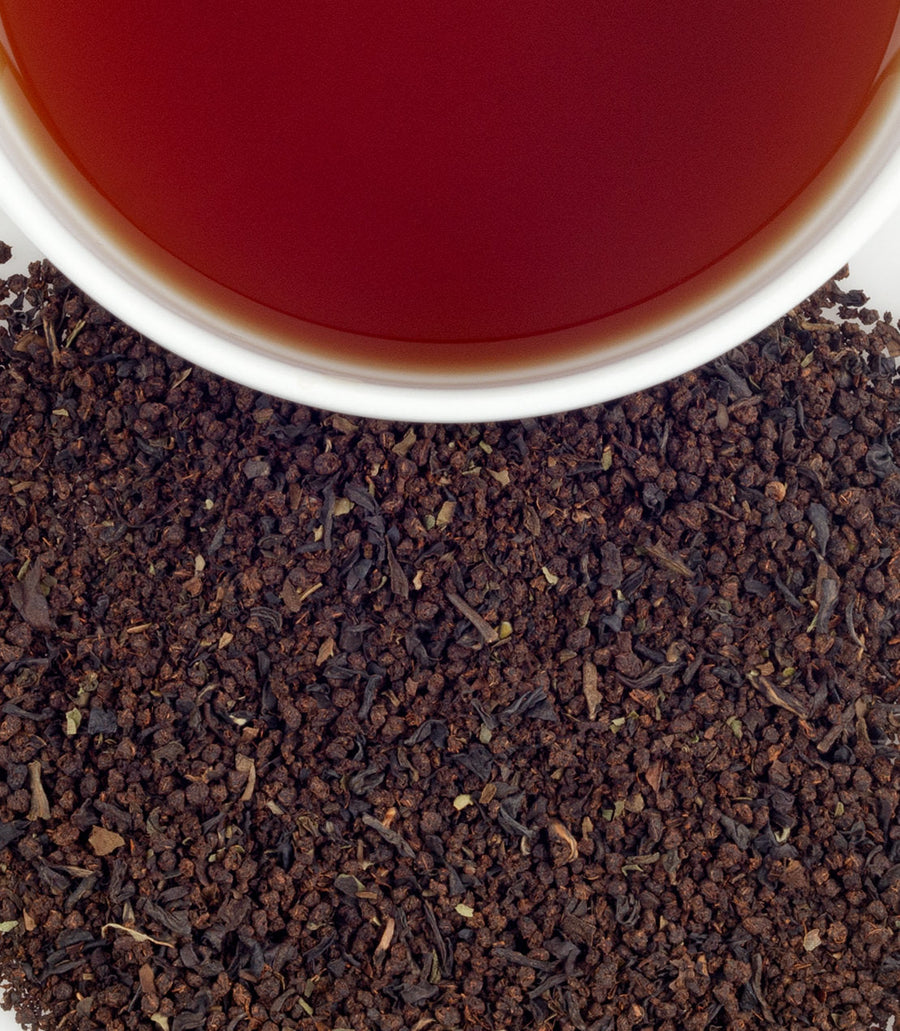 Close-up of tea leaves with a cup of tea in the background